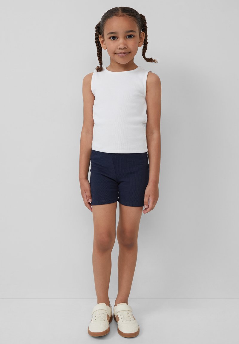 Weißes geripptes Tanktop, marineblaue Shorts und cremefarbene Sneakers. Das Outfit weist ein einfaches, tailliertes Design auf, das sich gut für die Freizeit eignet.