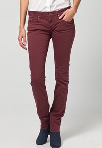 Pantalones ajustados burdeos de algodón con una textura suave; cuentan con bolsillos delanteros y cierre con botón. Combinados con botines al tobillo.