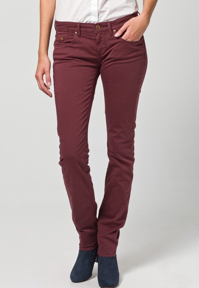 Pantalones ajustados burdeos de algodón con una textura suave; cuentan con bolsillos delanteros y cierre con botón. Combinados con botines al tobillo.
