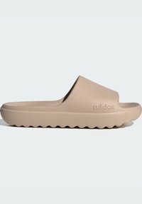 Beige slidesandal i texturerad gummi, med en bred rem och en vågig sula för grepp. "adidas"-logotyp prägla på sidan.