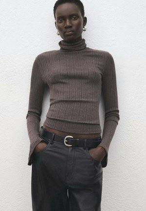 Smeđi rebrasti pulover s dubokim okruglim izrezom i dugim rukavima, upareni s crnim kožnim hlačama i crnim remenom sa srebrnom kopčom.