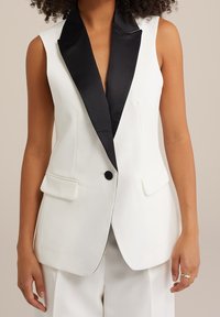 Vit ärmlös blazer med krage i svart satin, framfickor, enkel stängning med svart knapp och en slät yta.