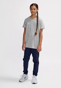 Grå t-shirt med korta ärmar och logotyp på bröstet, kombinerad med marinblå byxor och vita sneakers. Mjukt tyg och avslappnad passform.