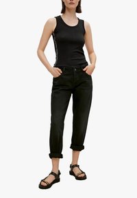 Top de tirantes negro acanalado con raya lateral, combinado con jeans de mezclilla negros remangados y sandalias negras gruesas con un acento de cadena.