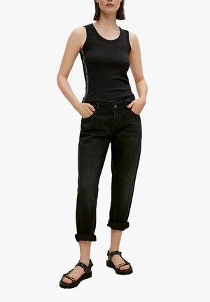 Débardeur noir à côtes avec une rayure sur le côté, associé à un jean en denim noir retroussé et des sandales noires épaisses avec un accent en chaîne.