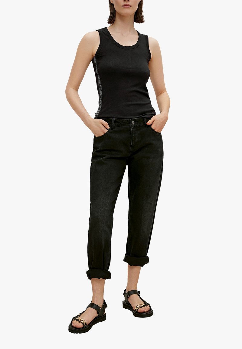Top de tirantes negro acanalado con raya lateral, combinado con jeans de mezclilla negros remangados y sandalias negras gruesas con un acento de cadena.