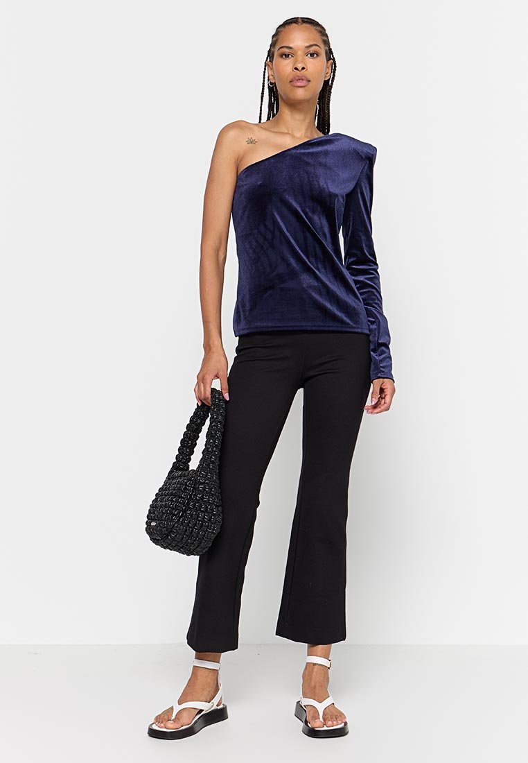 Marineblaues, einseitiges Samtoberteil mit strukturiertem Finish, kombiniert mit figurbetonten schwarzen Schlaghosen und einer geflochtenen schwarzen Tasche; Modell trägt weiße Sandalen.
