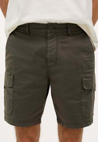 Pantaloni scurți cargo de culoare verde închis, cu o croială lejeră, având buzunare laterale, închidere cu buton și benzi pentru curea. Construiți dintr-un material rezistent, cu o textură netedă.