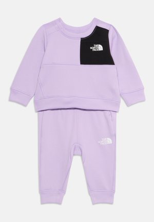 Ensemble de survêtement lilas en tissu doux ; comprenant des manches longues, un patch noir sur la poitrine et un logo blanc sur le pantalon. Poignets élastiques aux manches et aux chevilles.
