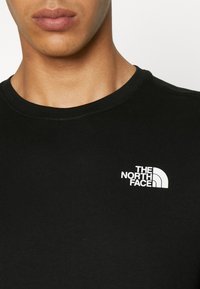 Black cotton t-shirt with a round neck and short sleeves. Features a white logo "The North Face" on the left side of the chest.