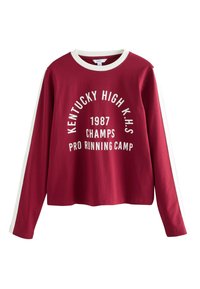 Punainen pitkähihaisen collegepaita, joissa valkoiset yksityiskohdat. Paidassa on valkoisella painettu teksti "KENTUCKY HIGH K.H.S 1987 CHAMPS PRO RUNNING CAMP" edessä.