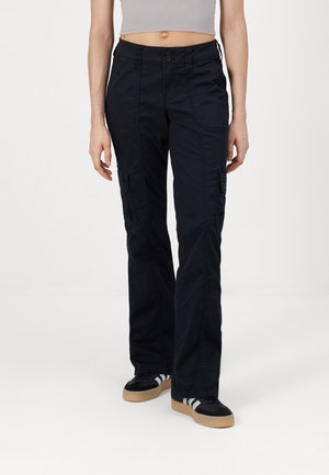 Pantaloni cargo neri con una vestibilità rilassata, dotati di tasche anteriori e laterali, chiusura a due bottoni e tessuto leggero. Abbinati a sneaker nere.