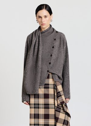 Grauer Strickpullover mit hohem Kragen, sieben dunklen Knöpfen entlang der Seite, kombiniert mit einem beigen karierten Rock mit braunen und schwarzen Akzenten.