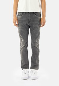 Jeans gris usés avec déchirures, dotés de cinq poches et d'une coupe droite classique. Associés à des baskets blanches pour le contraste.