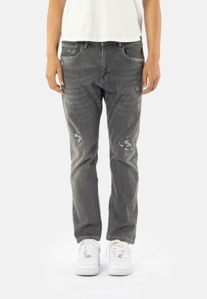 Grijze beschadigde jeans met scheuren, voorzien van vijf zakken en een klassieke rechte pijp. Gepaard met witte sneakers voor contrast.