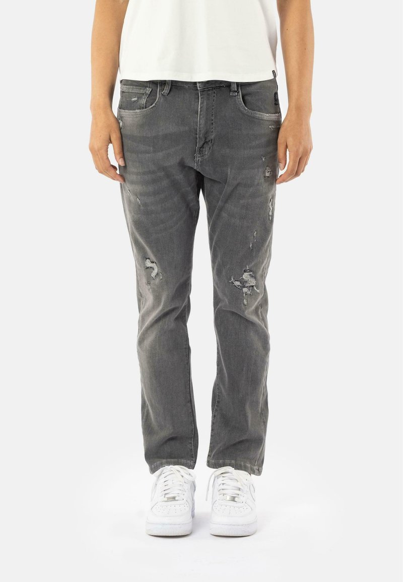 Jeans gris usés avec déchirures, dotés de cinq poches et d'une coupe droite classique. Associés à des baskets blanches pour le contraste.