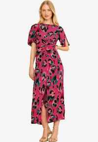 Roosa leopardimustriga kleit lühikeste libisevate varrukatega, sõlmitud vöökoha detailiga ja reie kõrguse sirge lõhekohaga. Komplektses koos kuldsete rihmadega sandaalidega.