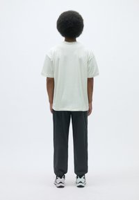 Lyse beige kortærmet t-shirt lavet af bomuld, parret med mørkegrå løse bukser. Sættet er fuldendt med multicolor træningssko.