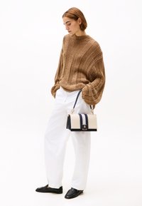 Brauner Pullover aus Strick mit Rippstruktur, weiße Hose, schwarze Slipper und eine zweifarbige Tasche mit creme- und marinefarbenen Streifen sowie goldener Hardware.