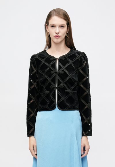 Veste en velours noir avec un design matelassé, fermetures à bascule à l'avant et manches longues. Associée à une jupe bleu clair.