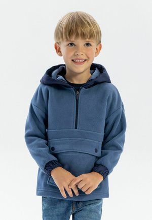 Felpa in pile blu con cappuccio blu navy, zip frontale a metà, polsini elasticizzati e tasca frontale con dettagli in bottone. Bambino che indossa jeans di denim.