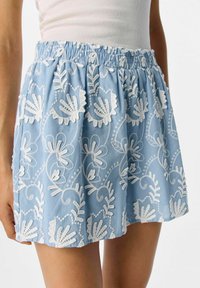 Jupe bleu clair avec broderies florales blanches, taille élastique, design froncé et tissu doux et texturé.