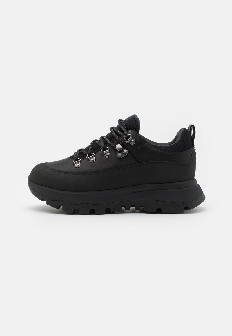 Black hiking shoe with a thick, textured sole, padded collar, metal eyelets, and matching laces. Material is smooth with a matte finish.