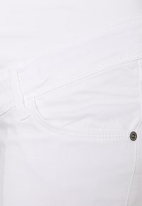 Tecido branco com costura visível, apresentando um bolso frontal e acabamentos em metal. Textura suave e design de denim padrão.