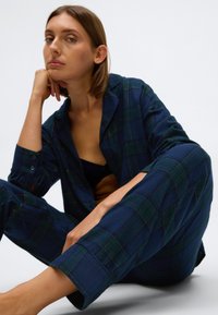 Navy geruite loungewear set in zachte stof met groene accenten. Geknoopte blouse en loszittende broek met opgerolde mouwen, casual ontwerp.