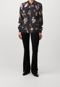Květinová bomber bunda z tmavé látky se zipem vpředu, žebrovanými manžetami a lemem. Celá zdobená velkými vícerozměrnými květinovými vzory.