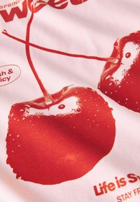 Cerezas rojas con reflejos blancos impresas sobre un fondo de tela rosa claro, con texto que dice "La vida es dulce."