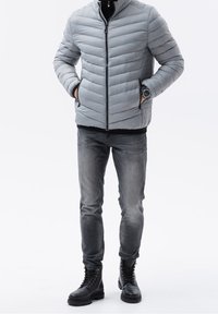 Szara pikowana kurtka puchowa z wysokim kołnierzem, zamkiem z przodu i bocznymi kieszeniami. Dobrana do ciemnoszarych jeansów i czarnych botków na sznurowadła.