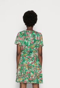 Bloemendress met een groene basis, voorzien van een meerkleurig bloemenpatroon, korte mouwen en een gelaagde rucheszoom.