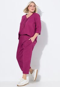 Dvoudílný outfit v jasné magentě, obsahující texturovaný, volný top s výstřihem do V a tříčtvrtečními rukávy, a odpovídající kalhoty s kapsami.