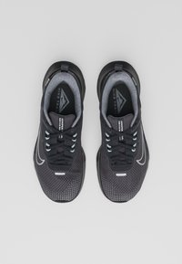 Black athletic shoes with a textured mesh upper, grey lining, and reflective accents. Features a thick sole and flat laces in light blue.