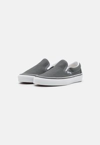 Baskets slip-on en toile grise avec semelles en caoutchouc blanches et détails noirs. Présente des accents élastiques sur les côtés pour un enfilage facile.
