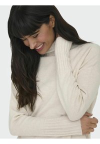 Pull en col roulé beige avec des poignets côtelés, fabriqué en tissu doux. Dispose de manches longues et d'une coupe ajustée, porté de manière décontractée.