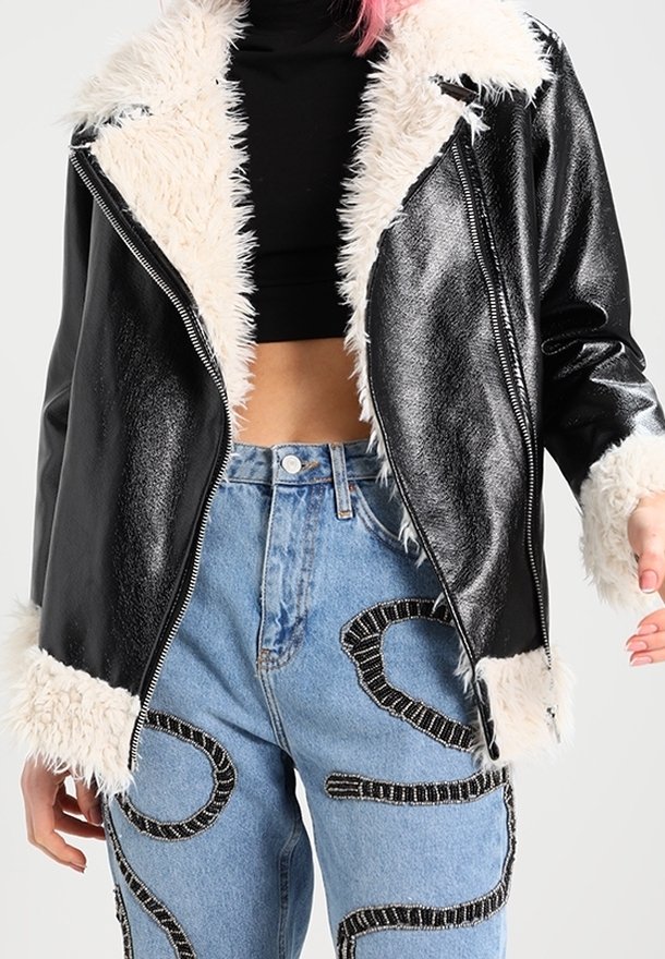 Svart faux läderjacka med mjuk krämfärgad faux pälskrage och manschetter, dragkedja framtill, kombinerad med ljusblå denimjeans med dekorativ sömnad.