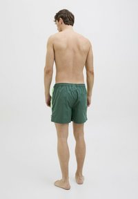 Groene zwemmershort met elastische tailleband, zijzakken en een achterzak. Gladde stof, lengte tot halverwege de dij, minimalistisch ontwerp.