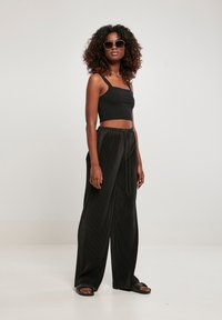 Must mustriga tank top ja mustad volditud laiad püksid, koos suurte ümmarguste prillidega ja mustade madala kontsaga sandaalidega. Sile tekstuur, lõdvene sobivus.