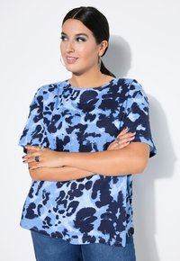 Oversized tričko s modro-navy abstraktním potiskem, kulatým výstřihem, krátkými rukávy a měkkou texturou, v kombinaci s denimovými džínami.