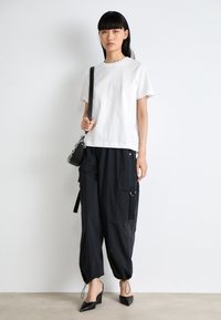 T-shirt en coton blanc associé à un pantalon cargo noir avec poches et poignets à cordon, complété par des talons aiguilles noirs et un petit sac à main.