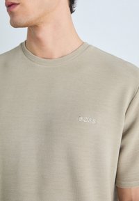 Béžové textúrované tričko s okrúhlym výstrihom a krátkymi rukávmi. Obsahuje vyšívané logo "BOSS" na ľavej hrudi.