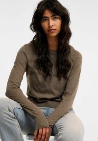 Olivgrön tröja med strukturerade bollar, rund halsringning och långa ärmar. Matchas med ljusblå denimjeans.