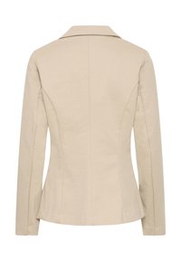 Blazer beige da donna su misura con maniche lunghe, cuciture strutturate e colletto con risvolto, vista da dietro su sfondo bianco.