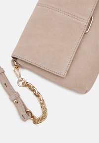 Semišová crossbody taška ve světle béžové barvě s magnetickým uzávěrem. Má zlatý chaîne a texturovaný, měkký povrch.