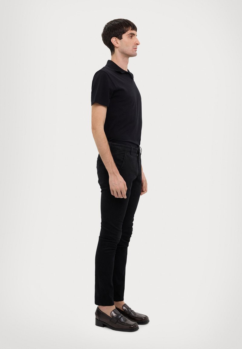 Polo noir avec col, pantalon noir slim-fit et mocassins marron foncé. Design simple, texture lisse et sans motifs ni accents visibles.