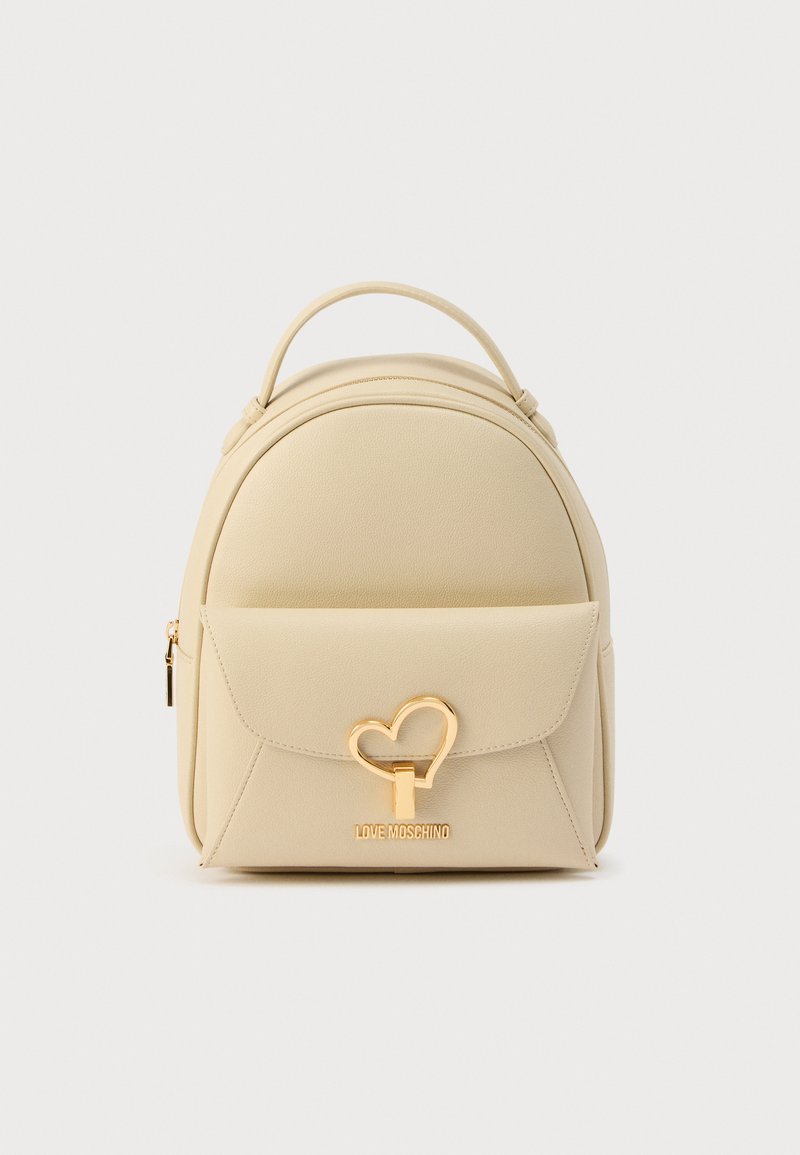 Σακίδιο πλάτης από μπεζ συνθετικό δέρμα με στρογγυλεμένο σχήμα. Διαθέτει μπροστινή τσέπη, χρυσά μεταλλικά στοιχεία σε σχήμα καρδιάς και ανάγλυφο λογότυπο της μάρκας.