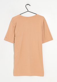 T-shirt a maniche corte di colore pesca in morbido cotone, con scollo rotondo e taglio dritto. Appesa a un gancio metallico nero.