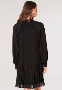 Schwarzes plissiertes Kleid mit langen Ärmeln und einer Knopfverschluss an den Ärmelbündchen, mit einem strukturierten Gewebemuster und fließendem Saum.